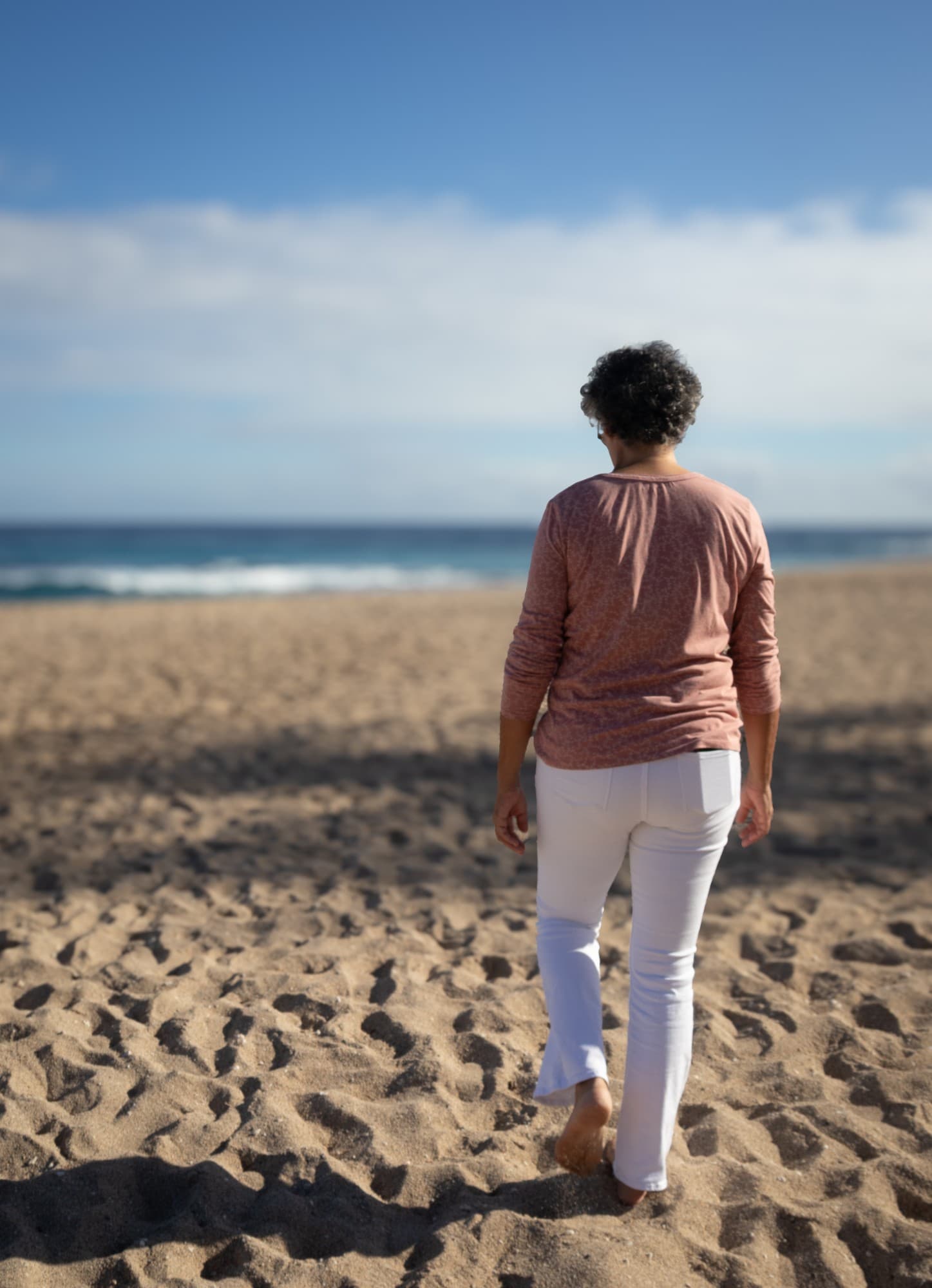 Valérie Patole de dos, pieds nus, qui marche vers la mer