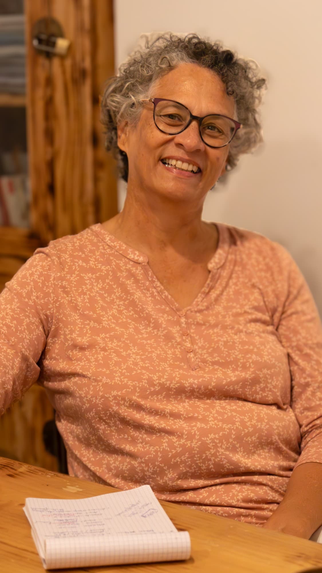 Portrait de Valérie Patole, souriante, assise à une table en bois